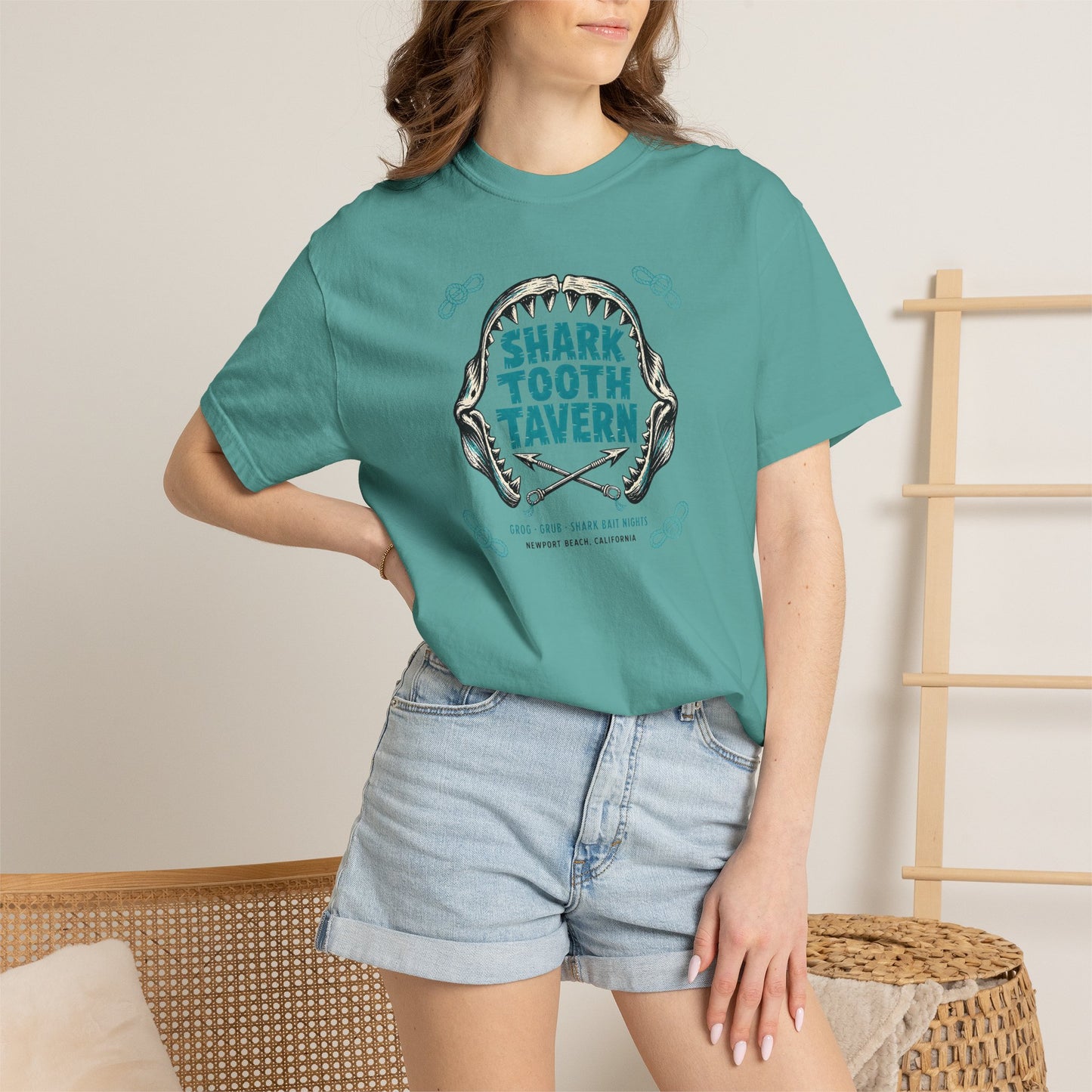 "Shark Tooth Tavern" — Newport Beach, California. Two inks, black and turquoise: a stylized shark-jaw arc with jagged carved teeth framing the venue name in bold tiki-block lettering, crossed harpoons...